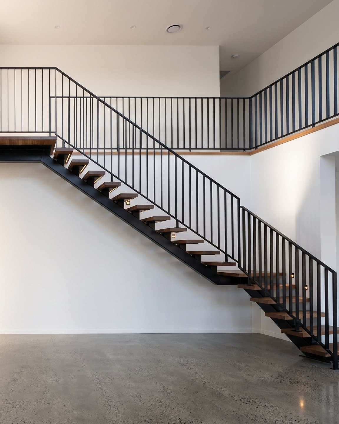 Sculptural black steel spine staircase with timber treads in a white void