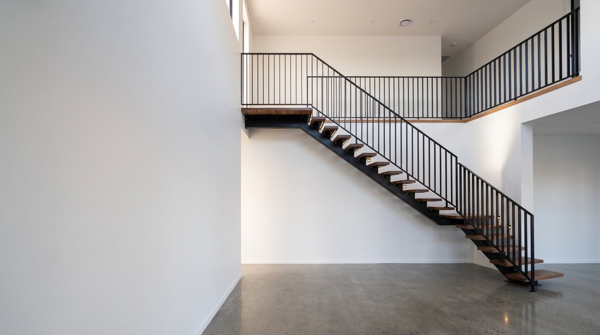 Sculptural black steel spine staircase with timber treads in a white void