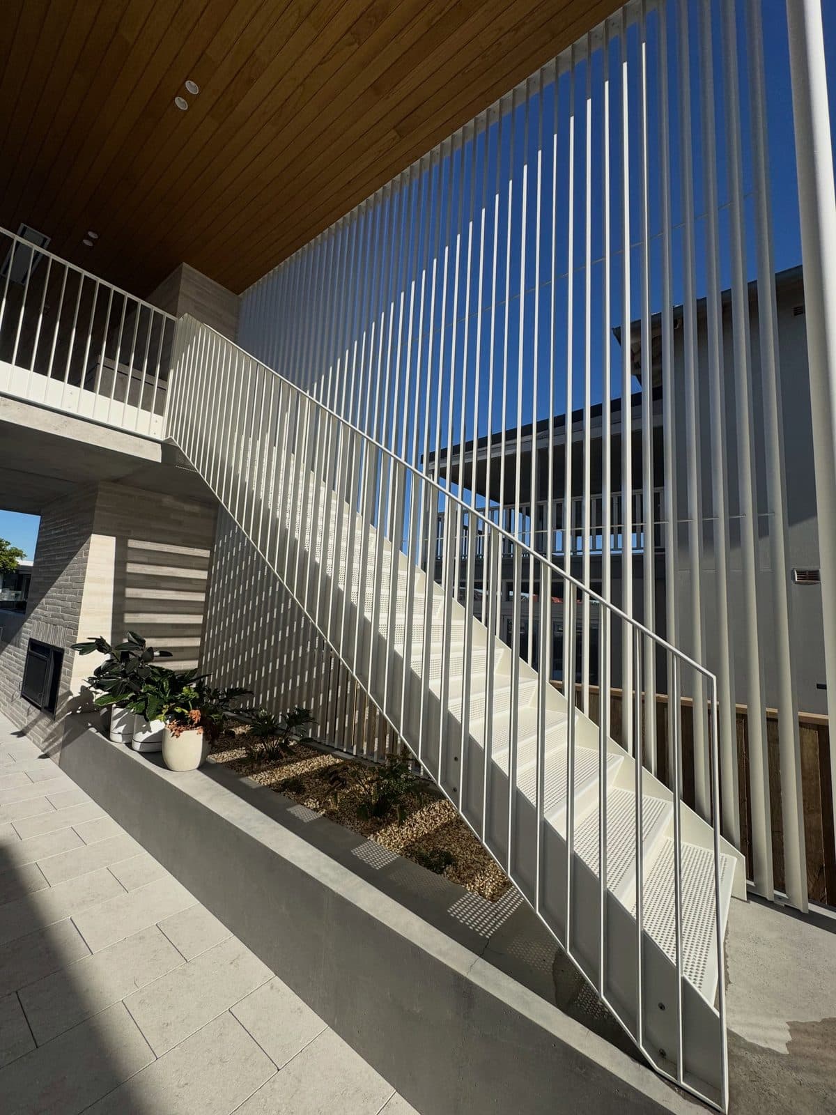 The stair from below — white steel against timber ceiling